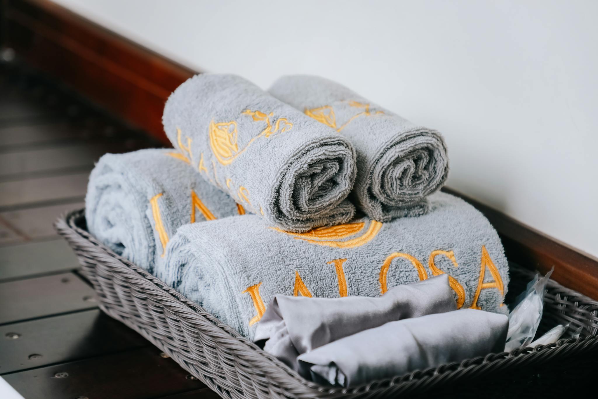 Close-up of neatly rolled gray towels with golden embroidery in a stylish wicker basket.